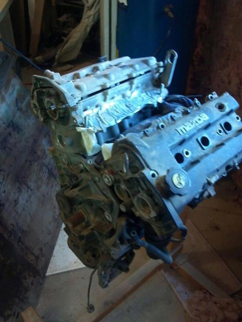1995 Ford Probe - A disassembled Mazda engine is shown from a 3/4 front angle, resting on a concrete floor. The engine block and valve cover are visible, wit…