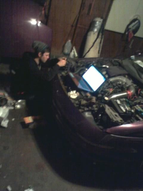 1995 Ford Probe - A person wearing a beanie works on the engine bay of a purple car, illuminated by a laptop screen.