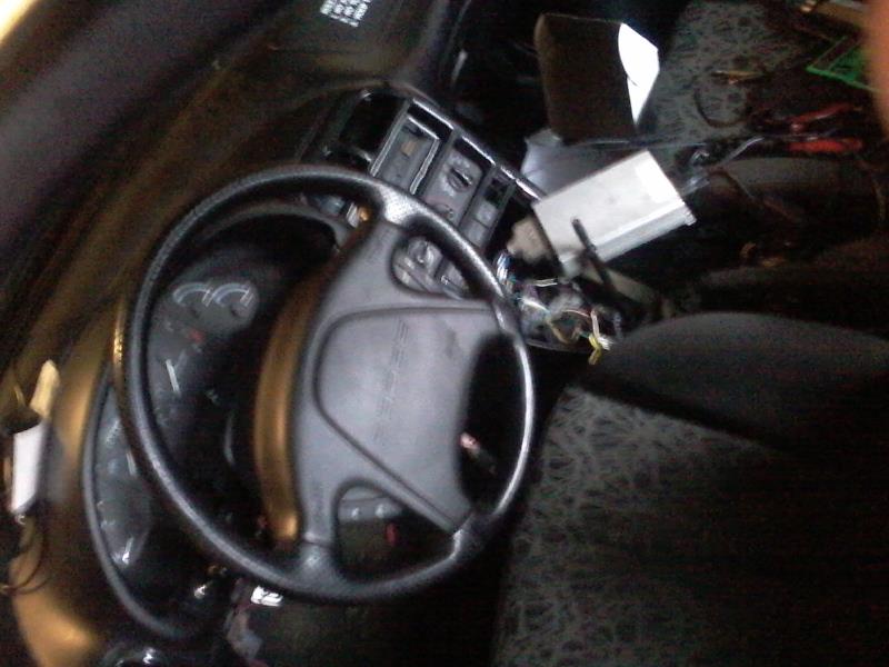 Car interior with steering wheel, dashboard, and visible wiring.