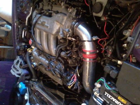 1995 Ford Probe - A close-up view of a modified engine bay, featuring a silver intake pipe with red bands and various wires and engine components. A Duracell…