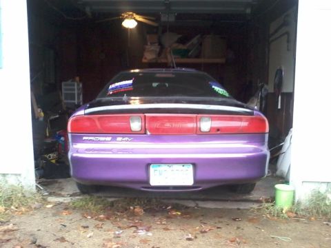 1995 Ford Probe - The rear view of a purple 1995 Ford Probe GT is parked in a garage. The car has aftermarket stickers on the rear window and a license plate…