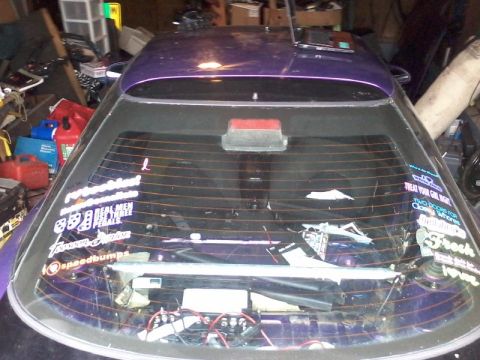 1995 Ford Probe - The rear of a purple hatchback with numerous stickers on the rear window. The interior of the car is visible through the window, showing wi…