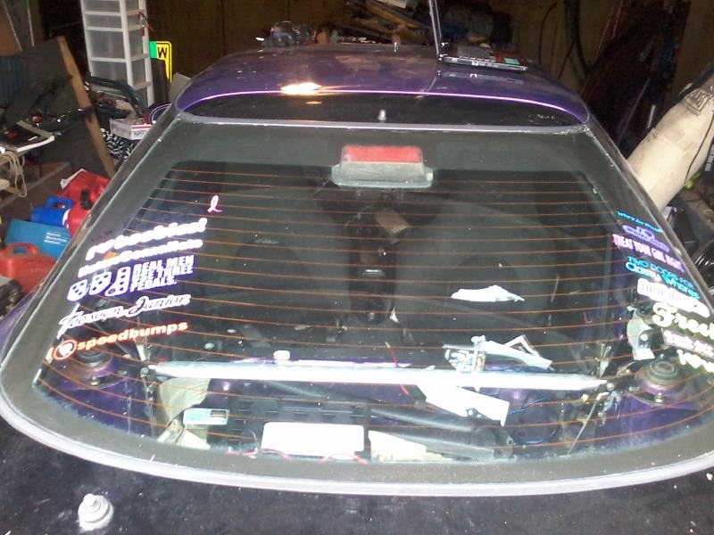 Rear window of a purple car with many stickers, parked indoors.