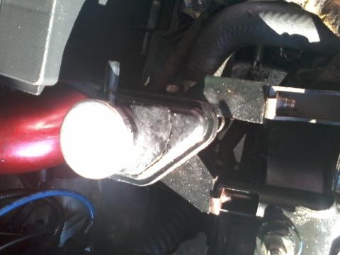 1995 Ford Probe - A close-up view shows a black metal bracket holding a cylindrical component with a white cap, likely part of a vehicle's engine bay. A red…