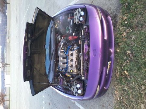 1995 Ford Probe - A high-angle, top-down view of a modified purple 1995 Ford Probe with its hood open, revealing the engine bay. The vehicle is parked outdoo…