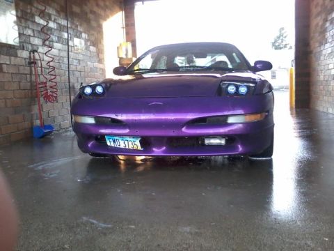 1995 Ford Probe - A purple Ford Probe is parked inside a car wash bay, with its headlights illuminated. The car's license plate reads "FMD 3735".