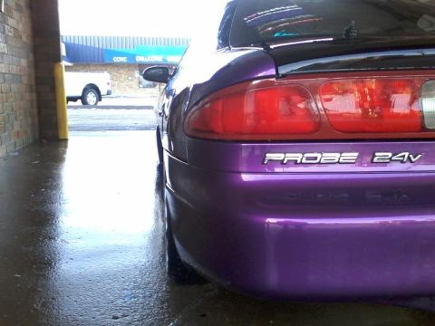 1995 Ford Probe - The rear quarter panel and taillight of a purple 1995 Ford Probe are visible in a car wash bay. The car has "PROBE 24V" badging on the rear.