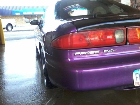 1995 Ford Probe - The rear passenger side of a purple 1995 Ford Probe is shown in a car wash bay. The car has a black spoiler and the text "PROBE 24V" is vis…