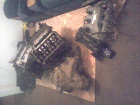 1995 Ford Probe - Two disassembled engine components, likely from a 1995 Ford Probe, are laid out on a piece of plywood. One component appears to be an intak…