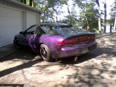 1995 Ford Probe - A purple 1995 Ford Probe is parked in front of a two-car garage. The rear driver's side of the car is visible, showing its taillights and a…