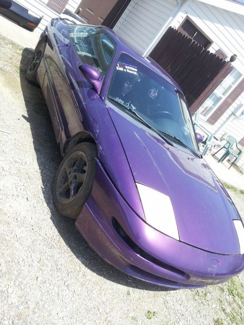 1995 Ford Probe - A purple 1995 Ford Probe is parked on a gravel surface in front of a building with a wooden fence. The car has pop-up headlights and a stic…