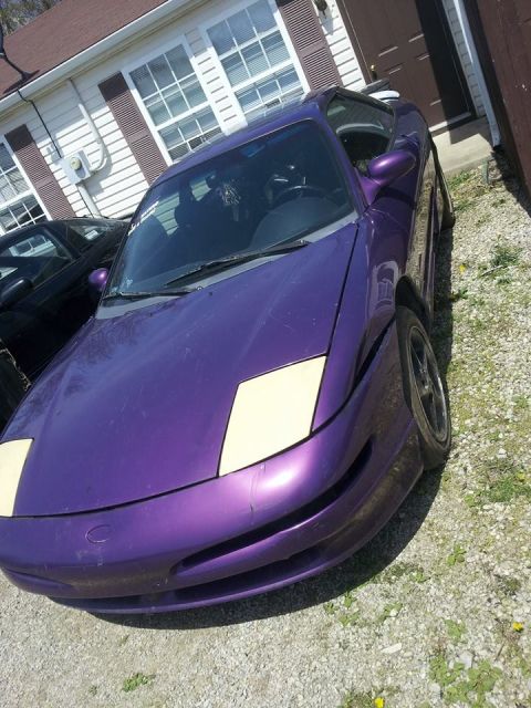 1995 Ford Probe - A purple 1995 Ford Probe is parked on a gravel driveway in front of a house. The car has pop-up headlights that are partially raised.