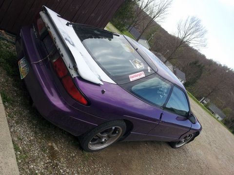 1995 Ford Probe - The rear passenger side of a purple 1995 Ford Probe is shown parked on a gravel lot next to a wooden structure. The car has a large white s…