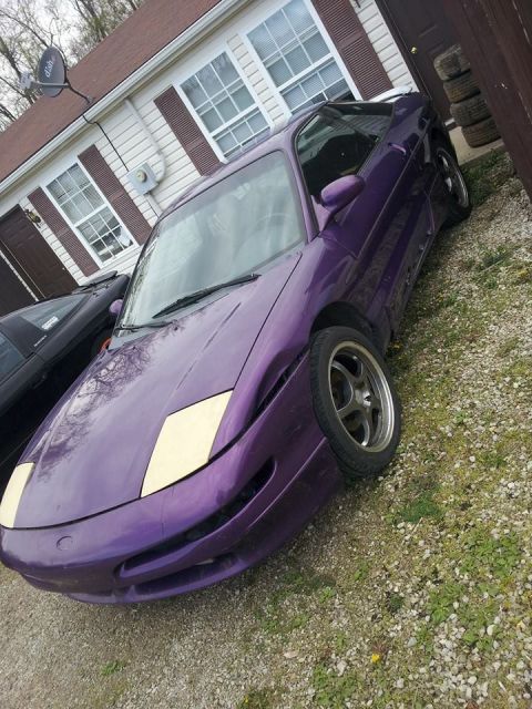 1995 Ford Probe - A purple 1995 Ford Probe is parked on a gravel driveway in front of a house. The car has a custom front bumper and pop-up headlights.