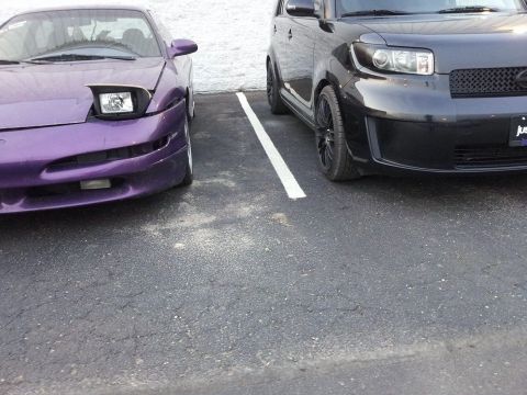 1995 Ford Probe - The front driver's side quarter of a purple Ford Probe is parked next to the front of a black Scion XB. Both cars are in a parking lot with…