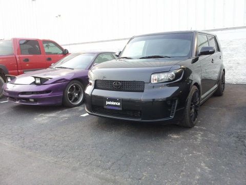 1995 Ford Probe - A black Scion xB is parked in front of a purple Ford Probe. The Scion has a license plate frame that reads "juststance".