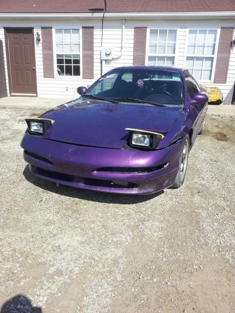1995 Ford Probe - A purple Ford Probe with pop-up headlights is parked in front of a white building with brown shutters and a brown door. The front bumper ap…