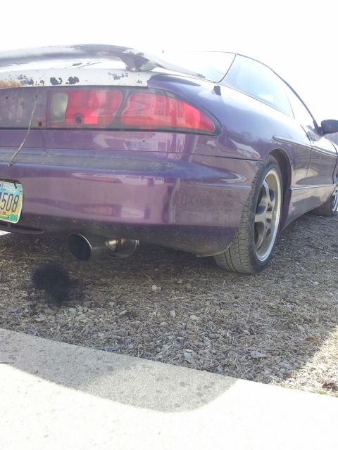 1995 Ford Probe - The rear driver's side of a purple 1995 Ford Probe is shown, parked on a gravel surface next to a concrete curb. The car has a custom exhau…