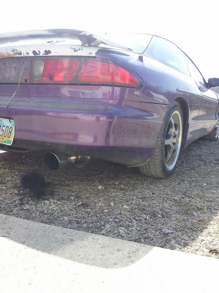 Purple 1995 Ford Probe, rear driver's side view, showing custom exhaust and rust.