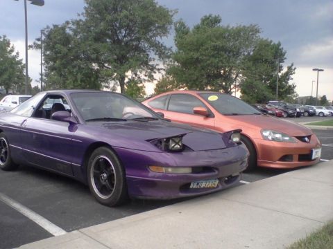 1995 Ford Probe - A purple 1995 Ford Probe is parked next to an orange car in a parking lot. The Probe has its pop-up headlights down and a license plate vis…