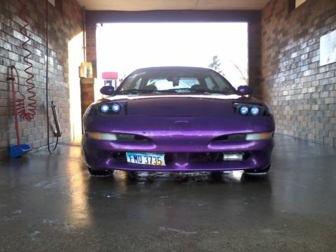 1995 Ford Probe - Front view of a purple 1995 Ford Probe with custom headlights and a license plate reading "FMO 3735" parked inside a car wash bay.