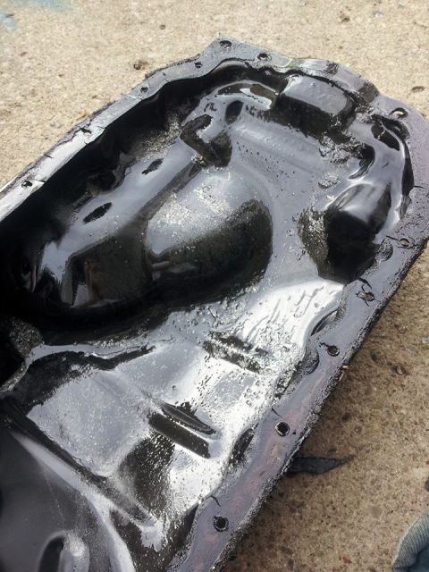 1995 Ford Probe - This is a close-up, overhead view of a dirty, black oil pan with a thick, black gasket and visible bolt holes. The pan is resting on a conc…