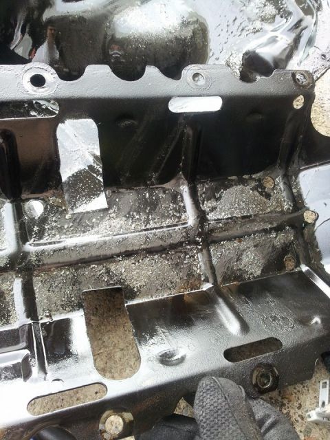 1995 Ford Probe - A black metal part, possibly an oil pan or underbody shield, is shown with a rough, textured surface and some visible grime and debris. The…