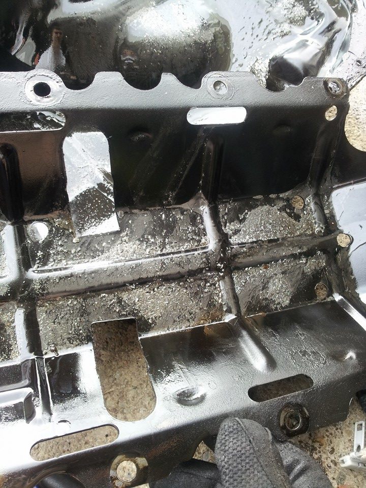 Black metal automotive part with cutouts and mounting holes, showing grime.