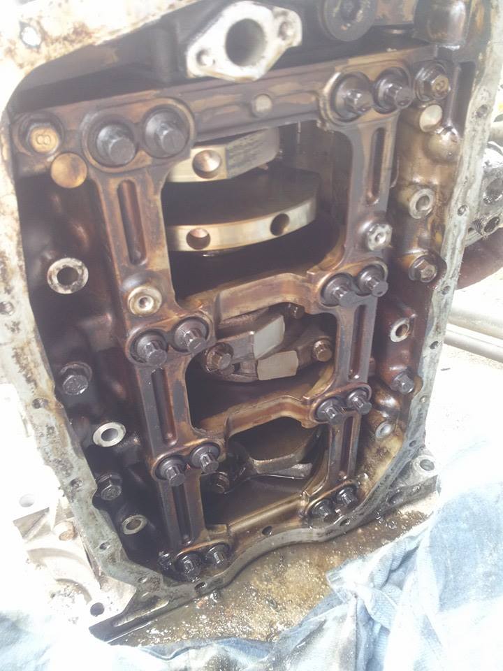 Close-up of dirty internal engine parts, crankshaft, and connecting rods.