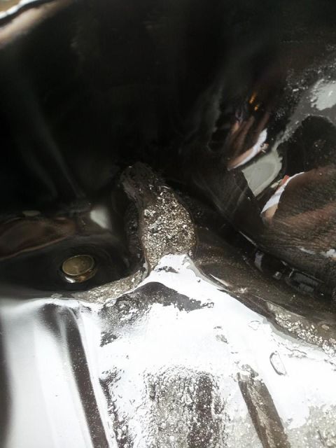1995 Ford Probe - A close-up view of the bottom of a vehicle's oil pan, showing a metallic drain plug and some accumulated grime and debris.
