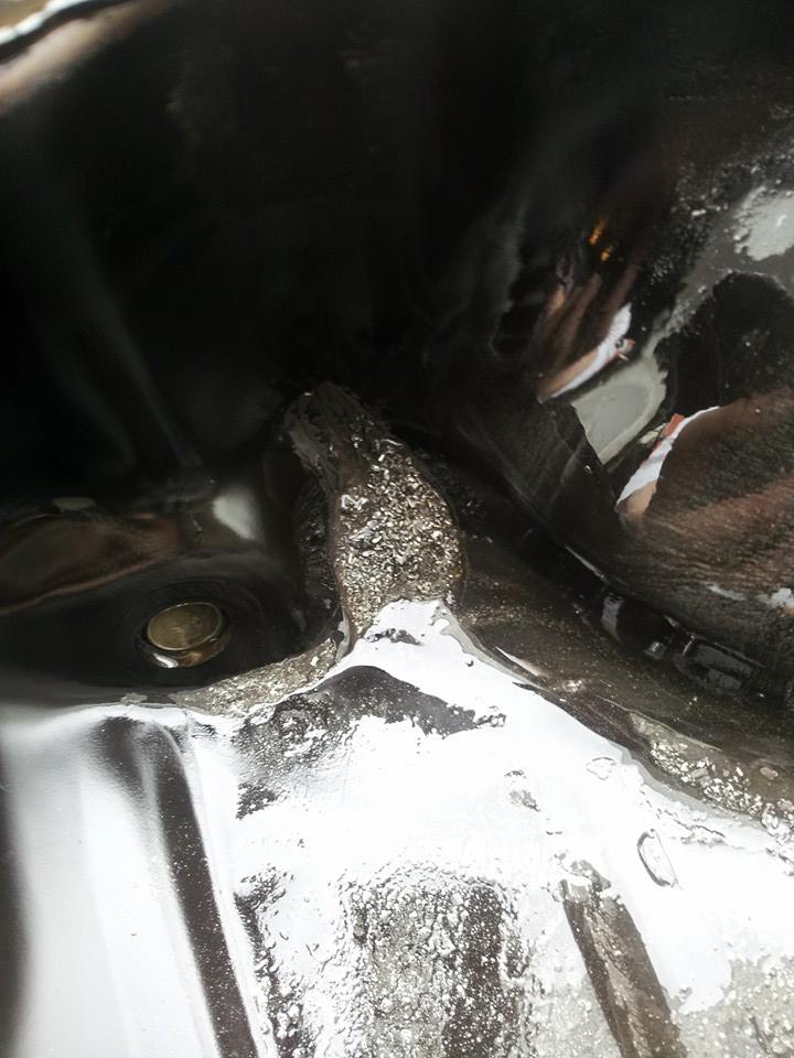 Close-up of a vehicle's oil pan with drain plug and debris.