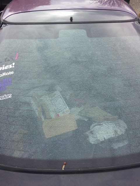 1995 Ford Probe - The rear window of a dark purple car is covered in a spiderweb pattern of cracks. Inside the car, a cardboard box and other debris are visi…