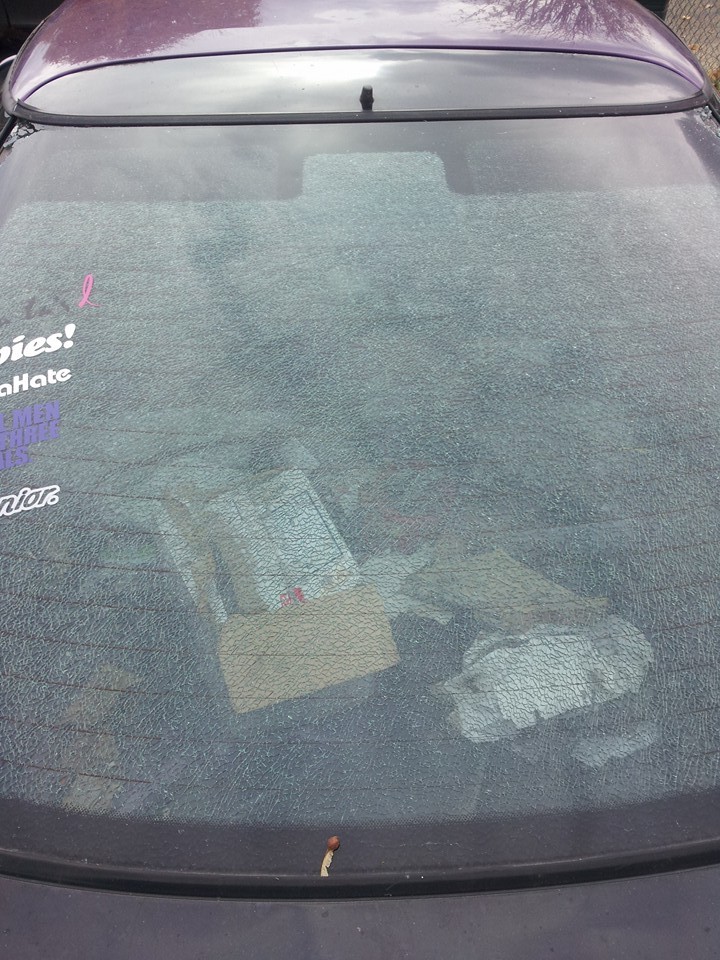 Cracked rear window of a dark purple car with debris inside.