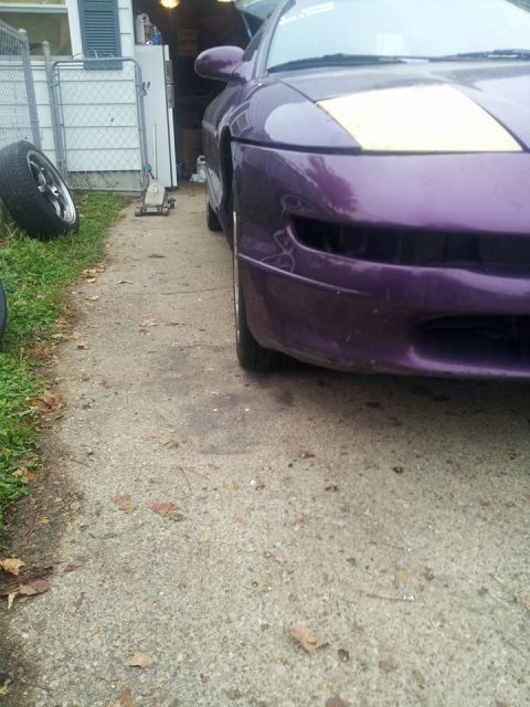 1995 Ford Probe - The front passenger side of a purple 1995 Ford Probe is shown parked on a concrete driveway next to a grassy area. A spare tire and a car j…