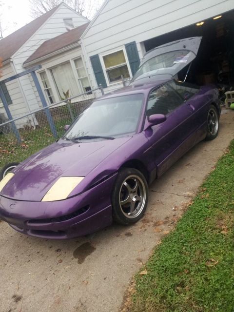 1995 Ford Probe - A purple 1995 Ford Probe with the trunk open is parked in a driveway next to a house. The car has aftermarket wheels and cream-colored head…