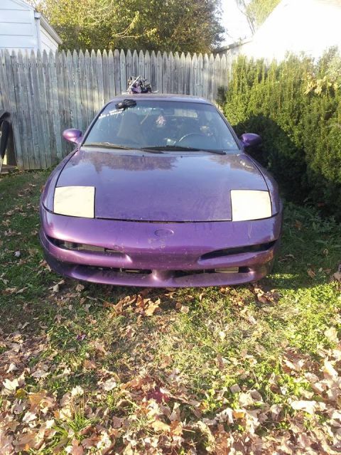1995 Ford Probe - Front view of a purple 1995 Ford Probe parked on a grassy lawn with fallen leaves. The car has pop-up headlights and a custom rack on the r…