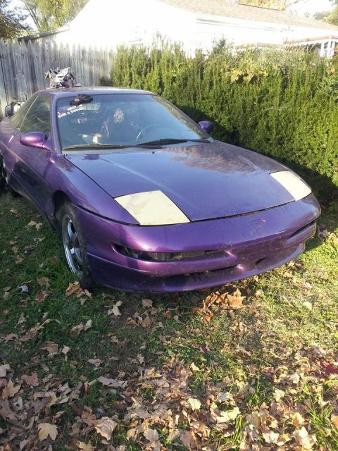 1995 Ford Probe - A purple 1995 Ford Probe is parked on a grassy lawn with fallen leaves around it. The car is viewed from a front three-quarter angle, with…