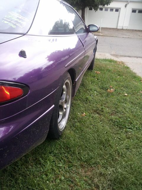 1995 Ford Probe - The rear passenger side of a purple 1995 Ford Probe is shown parked on a grassy area next to a driveway. The car has aftermarket wheels and…