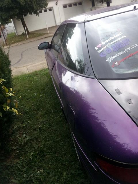 1995 Ford Probe - A side view of a purple 1995 Ford Probe with several stickers on the rear window. The car is parked on a grassy area next to a driveway and…