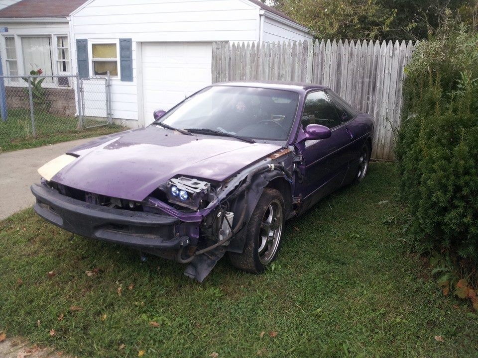 Damaged purple 1995 Ford Probe with missing front bumper and headlight.