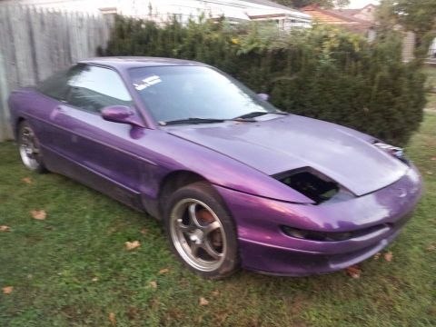 1995 Ford Probe - A purple 1995 Ford Probe is parked on a grassy lawn with a wooden fence behind it. The car's driver-side front headlight assembly is missin…