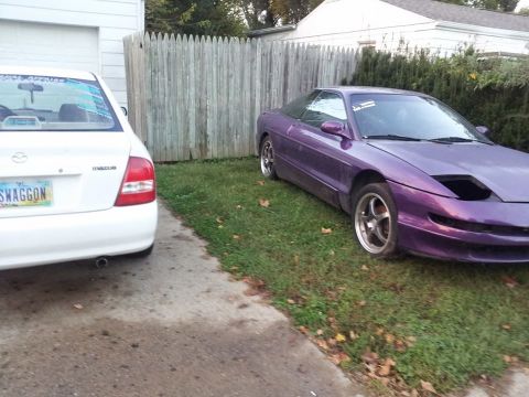 1995 Ford Probe - A purple 1995 Ford Probe is parked on the grass next to a white Mazda sedan. The Ford Probe has its headlights in the down position and is…