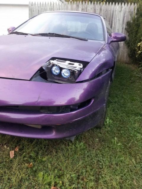 1995 Ford Probe - Front quarter view of a modified purple 1995 Ford Probe with its hood open, revealing aftermarket projector headlights. The front bumper ap…