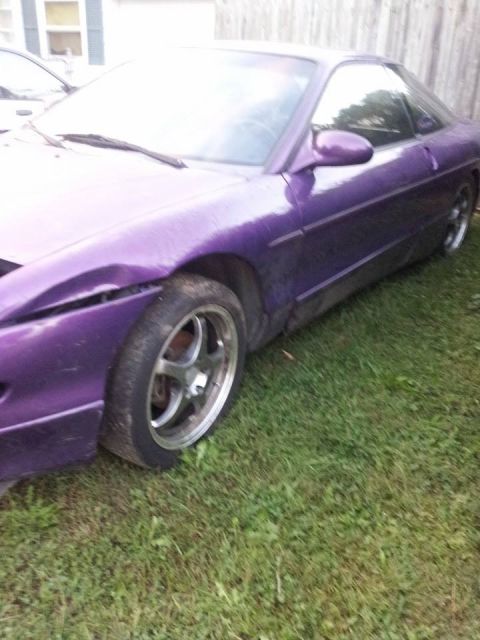 1995 Ford Probe - A damaged purple 1995 Ford Probe is parked on a grassy lawn with a wooden fence in the background. The front fender and bumper are visibly…