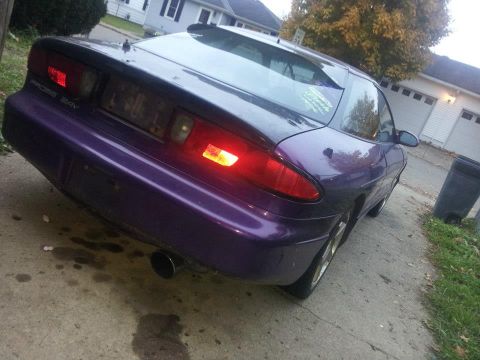 1995 Ford Probe - The rear driver's side of a purple 1995 Ford Probe is shown from a low angle, parked on a concrete driveway in front of a residential garag…