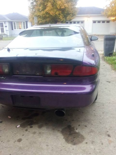 1995 Ford Probe - The rear passenger side of a purple 1995 Ford Probe is shown parked on a concrete driveway. The car has a spoiler and a visible exhaust pip…