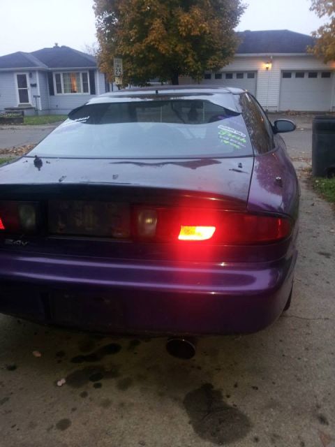 1995 Ford Probe - The rear passenger side of a purple 1995 Ford Probe is shown parked on a concrete driveway. The car has a spoiler, a cracked rear window, a…