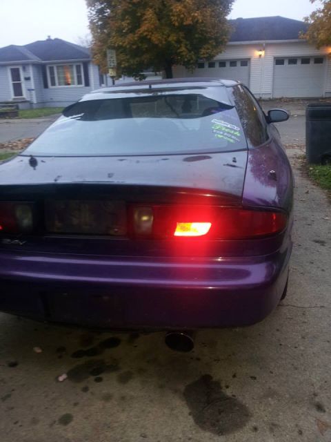 1995 Ford Probe - The rear passenger side of a purple 1995 Ford Probe is shown parked on a concrete driveway. A sticker with green text is visible on the rea…