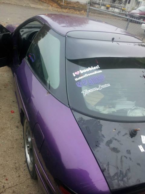1995 Ford Probe - The rear passenger side of a purple 1995 Ford Probe is shown with several stickers on the rear window. The car is parked on a concrete driv…