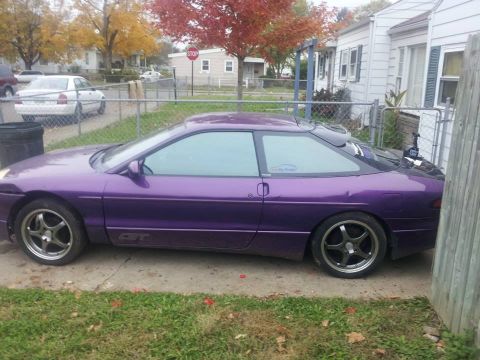 1995 Ford Probe - A side view of a purple 1995 Ford Probe GT parked on a concrete driveway with grass and a wooden fence in the background. The car has after…